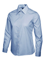 Light blue button-down shirt for women. Long sleeves, classic collar, and tailored fit. White buttons.